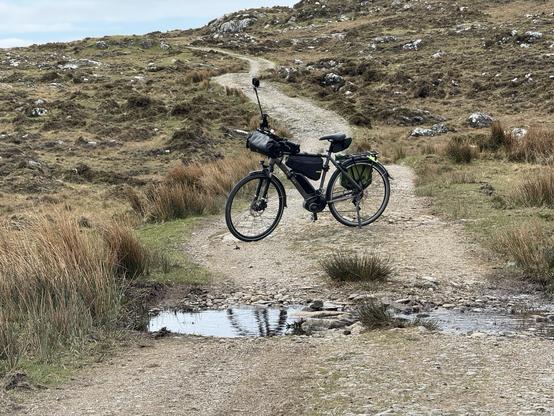 An ebike sideways on sits across a very rough & steep gravel descent to a narrow ford