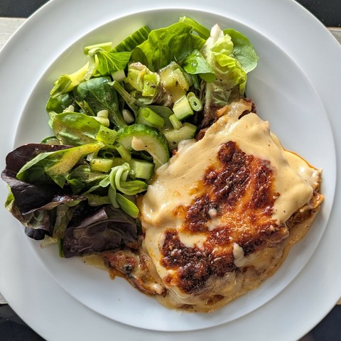 White plate, wedge of lasagna with the top slightly slipping, pile of dresed salad greens