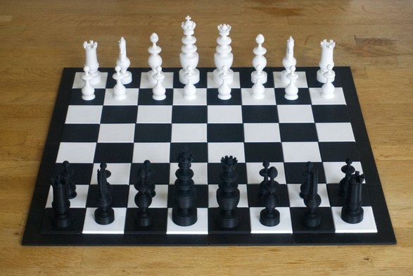 A 3D printed chess set and chess board on a tabletop. The set is bright white and coal black.