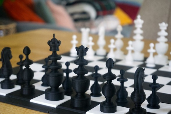 A 3D printed chess set and chess board on a tabletop. The set is bright white and coal black.