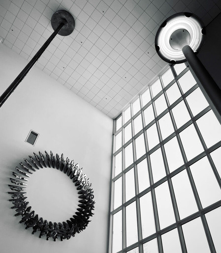 A ceiling view featuring a modern light fixture, a tall pole, and an artistic circular sculpture against a large window backdrop.