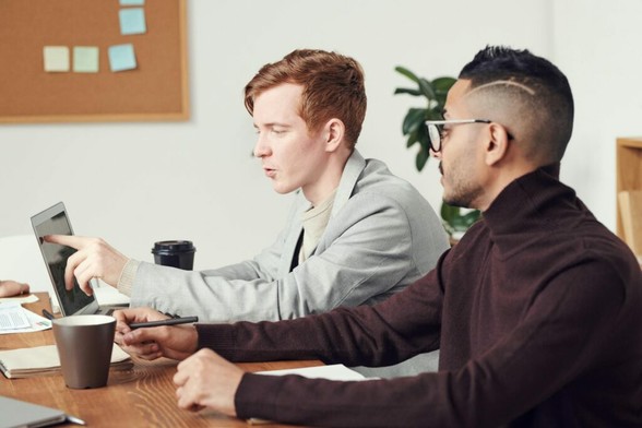 2 mannen zitten achter een laptop, 1 man wijst naar het scherm