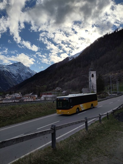 Foto. Berglandschaft mit Dorf und einem gelben Bus.