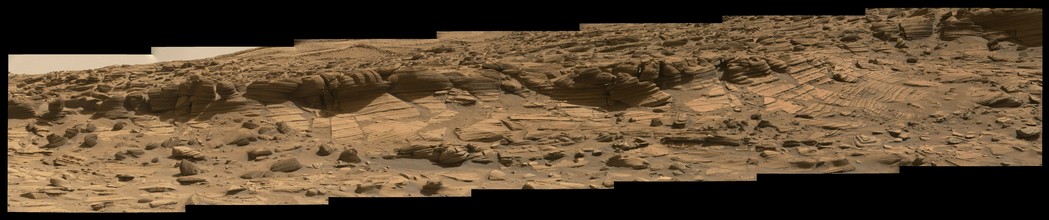 A rust toned mosaic of seven images stitched together horizontally, capturing the edge of the little canyon explored by the Mars rover Curiosity.