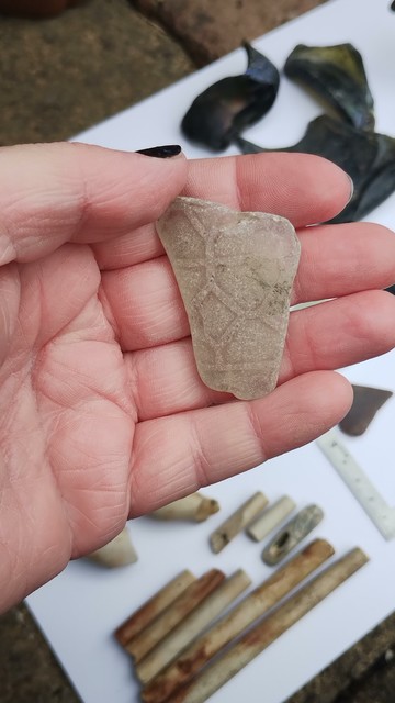 A hand holding a chunk of weathered glass that has a geometric pattern on it