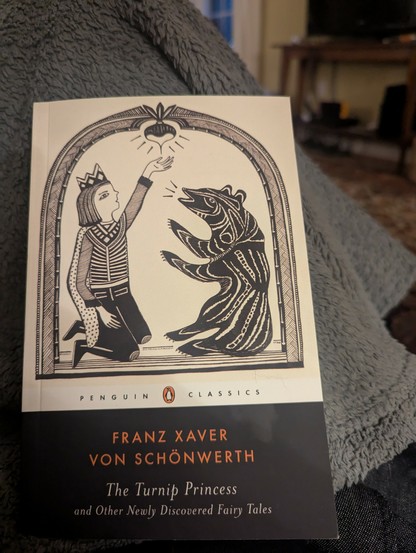 Picture of a book with cover art that's a wood cut block print of the Prince and the bear from the fairytale The Turnip Pribcess. Book title: The Turnip Princess and Other Newly Discovered Fairytales