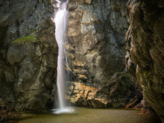Das Bild zeigt einen Wasserfall, durch den sich das Wasser in einer großen Fallstufe nach unten bewegt. Die Szene ist in goldenes Licht getaucht.