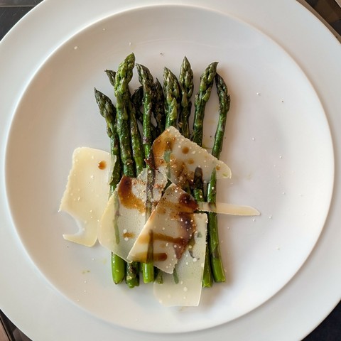 White plate, row of green asparagus spears and shavings of parmesan drizzled with balsamic vinegar