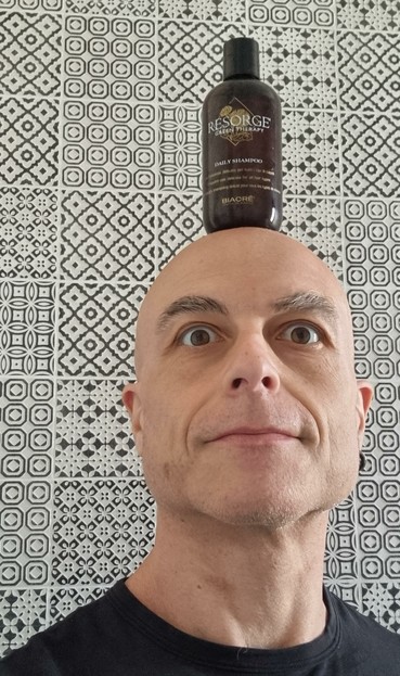 A man with a bottle of "Resorge" shampoo on top of his bald head.