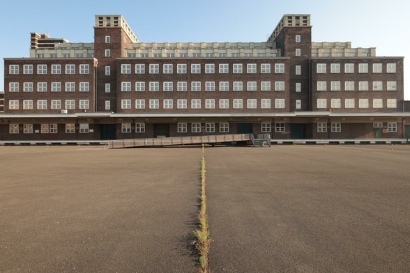 Gebäude im Stil Bauhaus. Eine Graslinie führt über den großen, geteerten, leeren Vorplatz auf die Mitte zu. Weiße, quadratische Fensterrahmen bilden zusammen mit dem symmetrischen Mauerwerk den Eindruck von Ordnung. Das Gebäude war einst das Hauptlagerhaus der Gutehoffnungshütte / Oberhausen und dient nun als Lagerhaus der LVR-Museen. Ordnung ist hier wichtig und die Form folgt der Funktion.