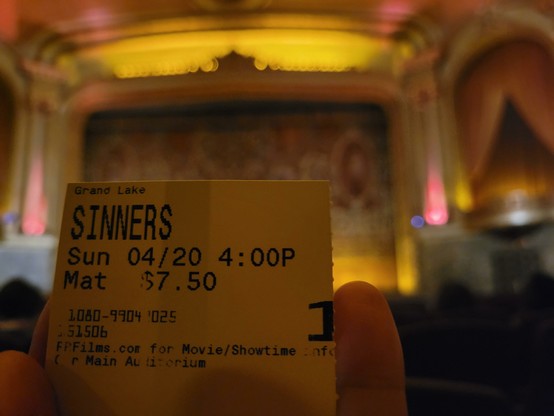 Photo of handheld movie ticket for movie Sinners 4:00 p.m. showing on Sunday, 4/20/2025 at the Grand Lake Theatre. The background shows the interior of the theatre before the movie.