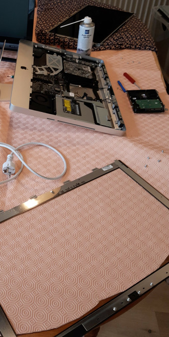 Photo de l'iMac démonté, vitre, chassis, disque dur et écrans  séparés. On voit un souffleur pour virer la poussière des ventilos.