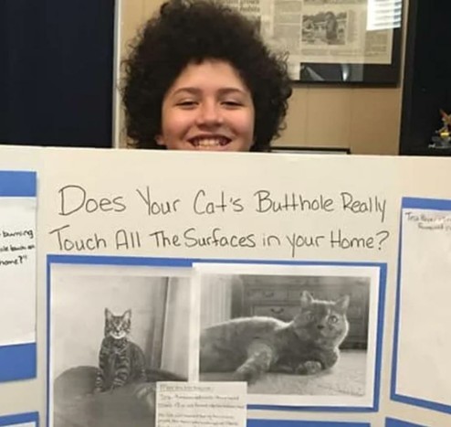 Child rocking an affro, holding up a science experiment titled "Does your cat's butthole really touch all the surfaces in your home?"