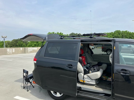 A black minivan with a magnetic antenna on top and a folding chair in the back, under an open door van.