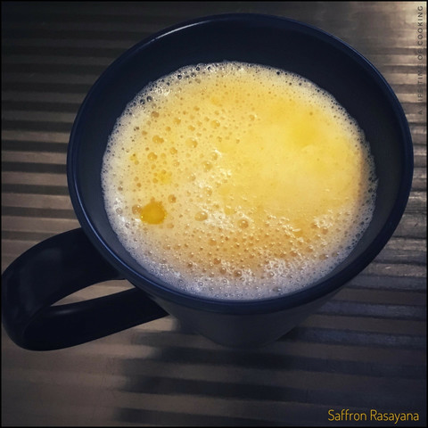 A coffee cup sits on a sink drain board and is filled with a hot, gold coloured drink.