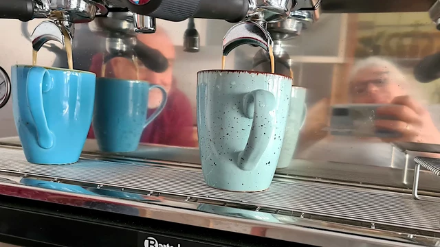 Siebträgermaschine hat spiegelndes Metall, man sieht die Frau mit Brille, die das Selfie erstelllte, links daneben einen Mann, der lächelnd zusieht wie der Kaffee einläuft.