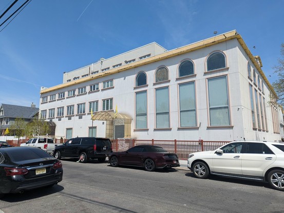 A large gurdwara. It is a white building. A covered doorway can be seen, with steps in front.
