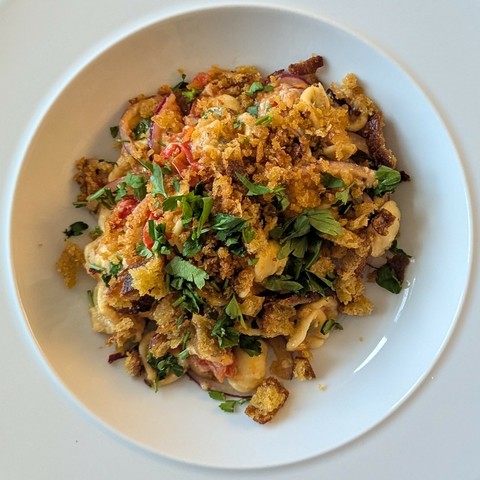 White bowl, golden pile of mixed small pasta with bits of tomato, red onion and parsley, breadcrumbs strewn over