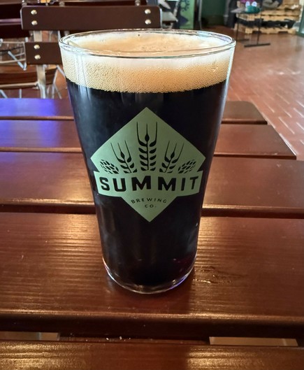 A pint glass full of dark beer with a thin tan head. The Summit beer logo is on n the center bar n light green colors, a diamond with clear lettering cutouts.