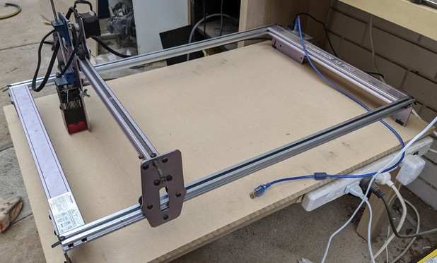 A laser cutter with mismatched sides, sitting in a messy carport