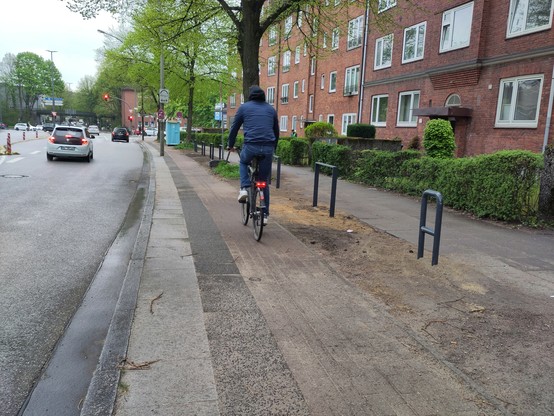 Das Bild zeigt den Radweg und Gehweg in der Steilshooper Straße, dazwischen einen unbefestigten Streifen mit Fahrradbügeln, auf dem bis vor Kurzem mit Anordnung geparkt wurde, obwohl der Streifen schmaler ist als jedes Auto.