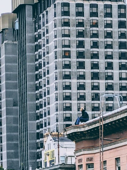 Person wearing headphones sitting on the roof with a skyscraper in the background