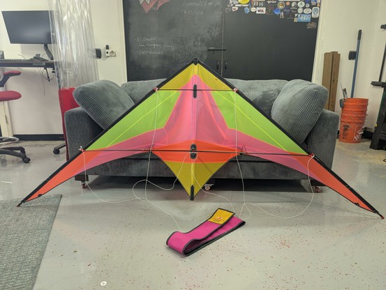 A prototype dual line sport kite with an applique sail in pink, orange, yellow, and florescent yellow standing upright in a workshop