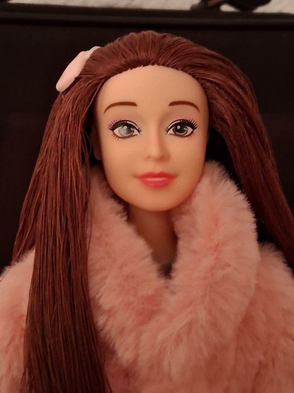 La muñeca de cerca. El cabello lo tiene hecho con hilo castaño y llega un pasador de color rosita y con forma de corazón. La cara tiene una expresión dulce e inocente