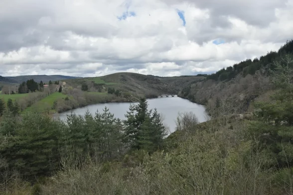Un petit lac légèrement enfoncé dans les montagnes avec un pont de quatre arches qui surplombe l'eau en arrière-plan. Le ciel est nuageux et la végétation semble sortir de l'hiver. Sur la droite, on perçoit quelques bâtiments sur les hauteurs d'un champ à l'herbe bien verte.