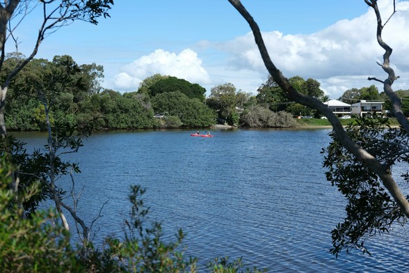 Two kayakers on the Currimundi Creek. There's green trees on both banks.