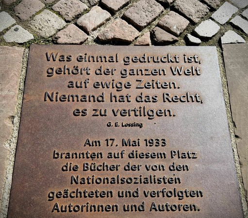 Was einmal gedruckt ist, gehört der ganzen Welt auf ewige Zeiten.
Niemand hat das Recht, es zu vertilgen.
©, E, Lessing
Am 17. Mai 1933
brannten auf diesem Platz die Bücher der von den Nationalsozialisten geächteten und verfolgten Autorinnen und Autoren.🖖