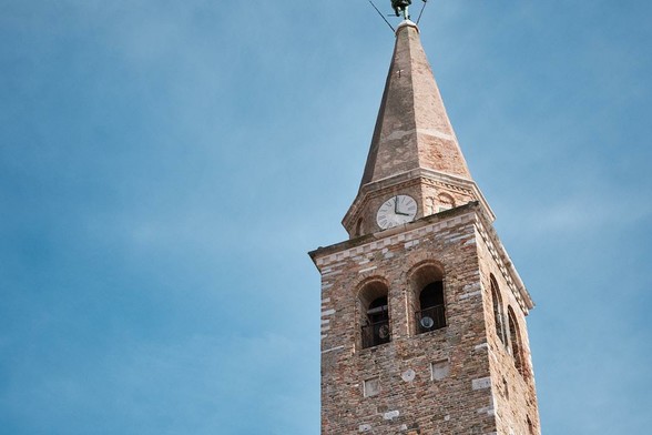 Brick church tower with a clock face and pointed spire against a clear blue sky.