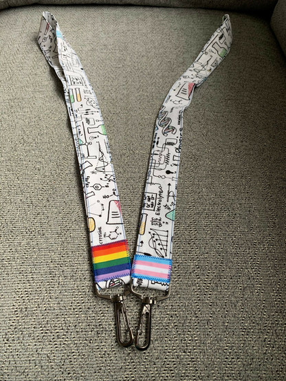 Two cotton lanyards covered in science type things, one with a standard pride flag at the end, one with a trans pride flag at the end.