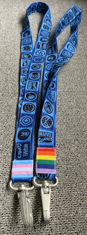 Two cotton lanyards covered in marvel comics symbols. One has a trans pride flag near the hook, and the other is a standard six stripe pride flag.