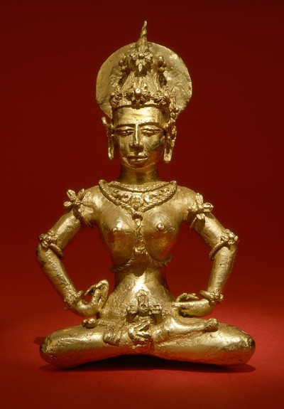 a seated figure made of gold, female, wearing jewelery, a tall crown and a halo-like disc behind the crown, the figure is in  a meditative position