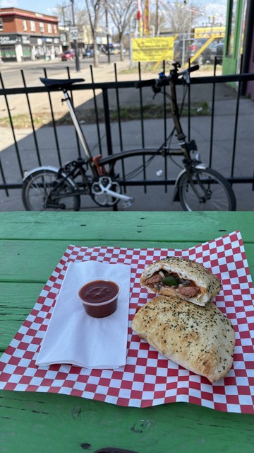 Fresh calzone cut in half in the foreground, Brompton bike locked to a fence in the background