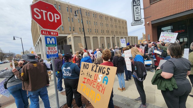 Protestors crowd on  a city street. A sign says No Kings In The USA. Impeach Trump.