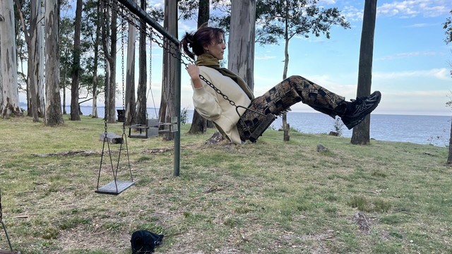 Una joven hamacándose en una espacio verde con un mar de fondo
