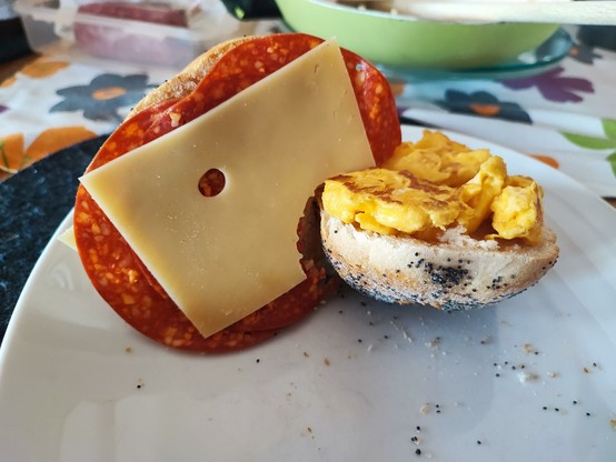 Abgebissene Salami-Käse-Brötchen-Hälfte sieht aus wie ein ein Kopf, welches in ein halbes Brötchen mit Rührei belegt beißt.