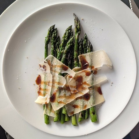 White plate, asparagus spears with shaved parmesan and a drizzle of balsamic