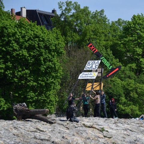 Ein Bohrturm direkt an der Isar (Reichenbachbrücke) mit der Message "Exit Fossils", "Koa Gas" und "Stoppt die Gasbohrungen" sowie Flaggen mit dem Logo von Extinction Rebellion. Hiermit soll auf die geplanten Gasbohrungen in Reichling am Ammersee aufmerksam gemacht werden.