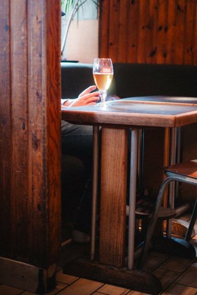 A table in a brown bar. There’s a beer on the table and the sun is shining through.