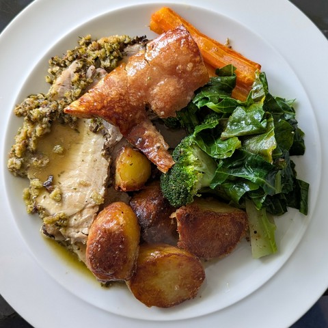White plate, slices of pork with herby edges, chunk of crackling, carrots, broccoli and cabbage, roast potatoes, gravy poured over