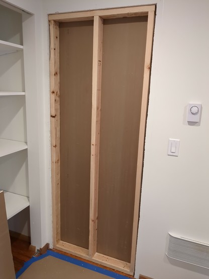 Wood framing filling an opening where an interior door used to be. The back side has brown sheetrock attached to it.