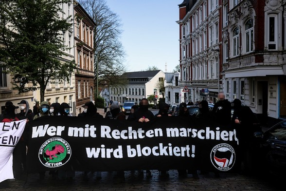Mehrere Menschen mit Transpis sind zu sehen. Die Menschen blockieren die Straße. Auf dem mittleren Transpi steht wer mit Rechten marschiert wird blockiert.