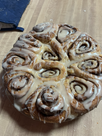 Photo of fresh baked glazed cinnamon rolls on a light wood countertop