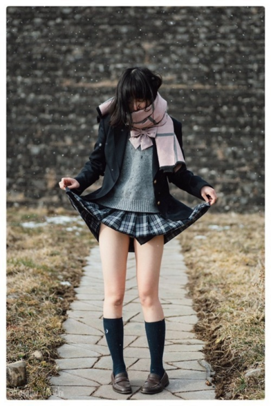 A young woman cosplaying as a Japanese Schoolgirl lifting her skirt giving just a glimpse of her knickers while light slow falls around her