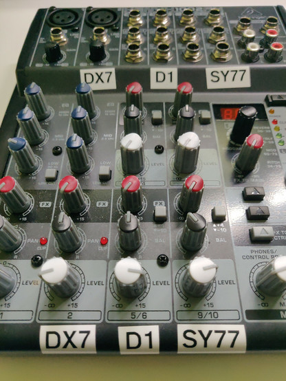 Detail eines kleinen Audio-Mischpults mit vielen Drehreglern und etwas schief angebrachten Labels für "DX7", "D1", "SY77".