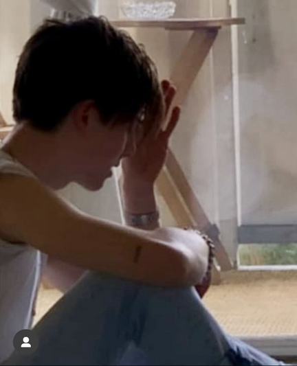 A young man sits on the floor wearing a white tshirt with the sleeves rolled up, a bracelet and watch.