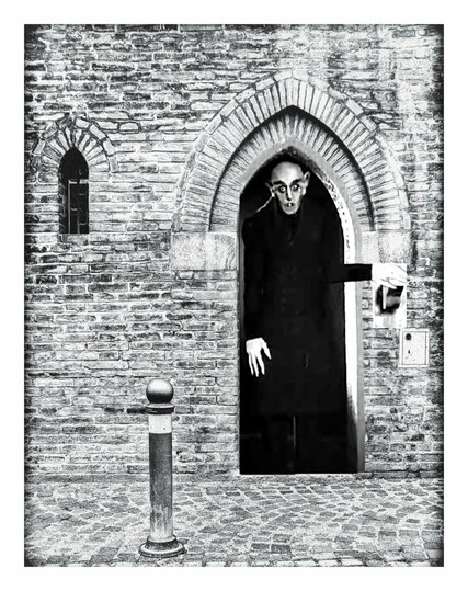 The same scene as previous. This time there is a tall, pale faced man (Count Orlock from Nosferatu) standing in the doorway with his hand on a light switch.